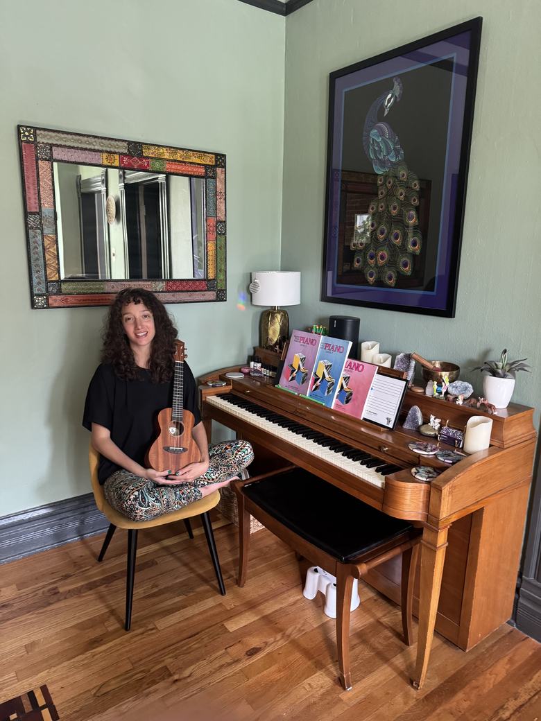 Erica Rosenblum in her Denver studio, seated by the piano with a ukulele